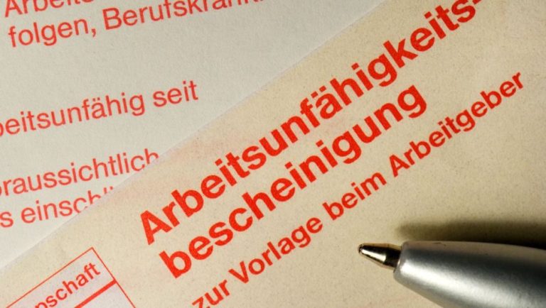 Arbeitsunfähigkeitsbescheinigung mit rotem Text und einem Stift daneben.